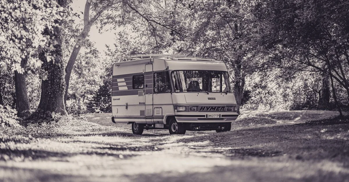 Un camping-car classique dans un cadre forestier tranquille, parfait pour les aventures en plein air.