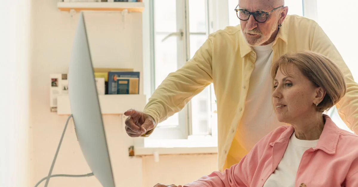 Couple âgé interagissant avec un ordinateur dans un cadre intérieur lumineux, collaborant et apprenant.